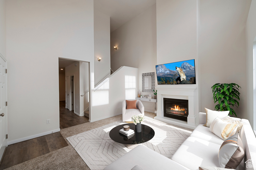 Living area with a glass covered fireplace, stairs, baseboards, a towering ceiling, and wood finished floors