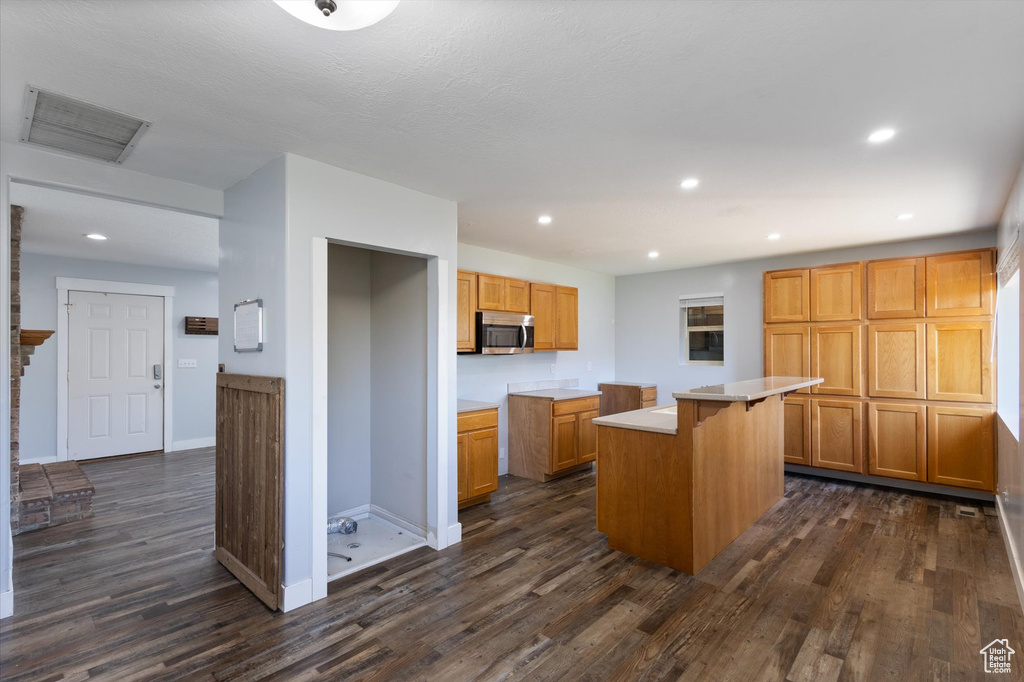 Kitchen with stainless steel microwave, dark wood-style flooring, a center island, recessed lighting, and baseboards