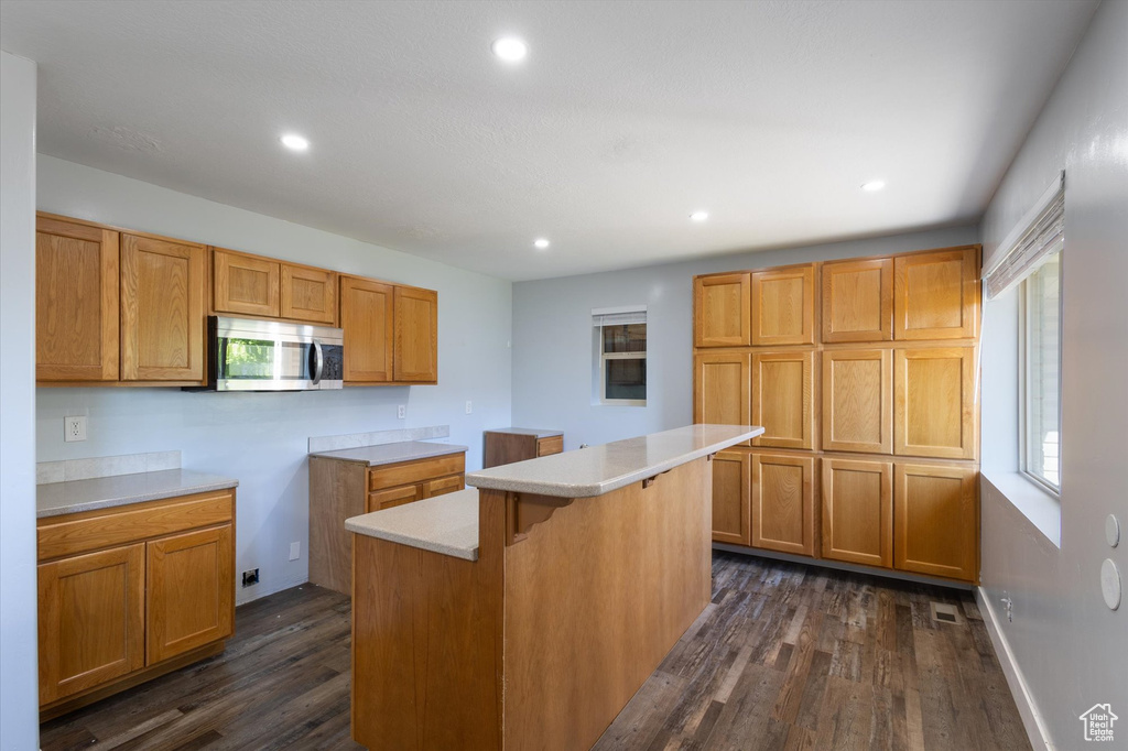 Kitchen featuring stainless steel microwave, dark wood finished floors, a breakfast bar area, a kitchen island, and recessed lighting