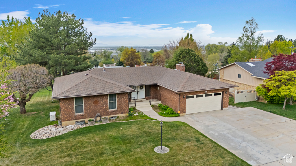 Ranch-style house featuring a shingled roof, brick siding, a garage, a front yard, and driveway