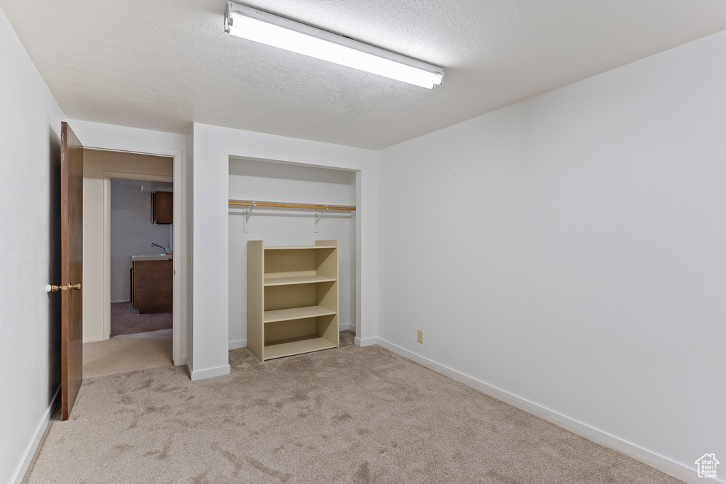 Unfurnished bedroom with a textured ceiling, baseboards, carpet, and a closet