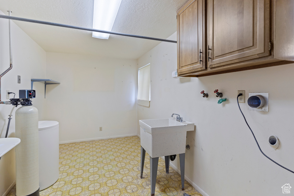 Clothes washing area with light floors, baseboards, washer hookup, and cabinet space