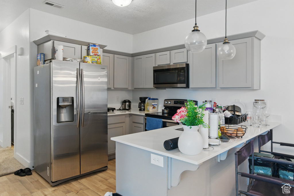 Kitchen featuring light wood finished floors, visible vents, a peninsula, gray cabinetry, and appliances with stainless steel finishes