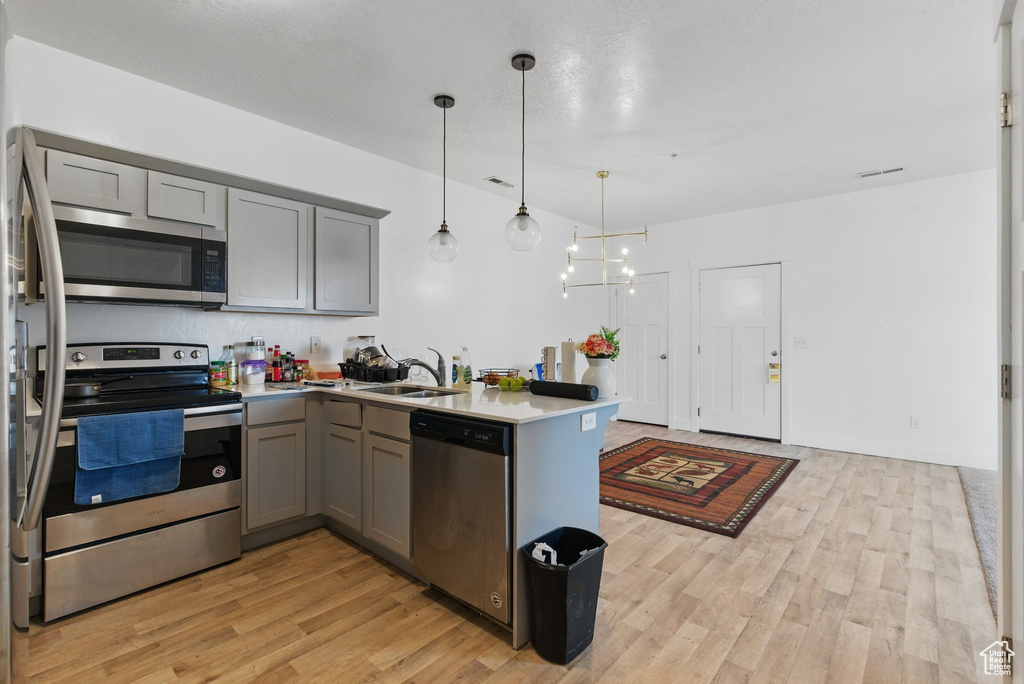 Kitchen featuring a sink, appliances with stainless steel finishes, light wood-style floors, a peninsula, and gray cabinets