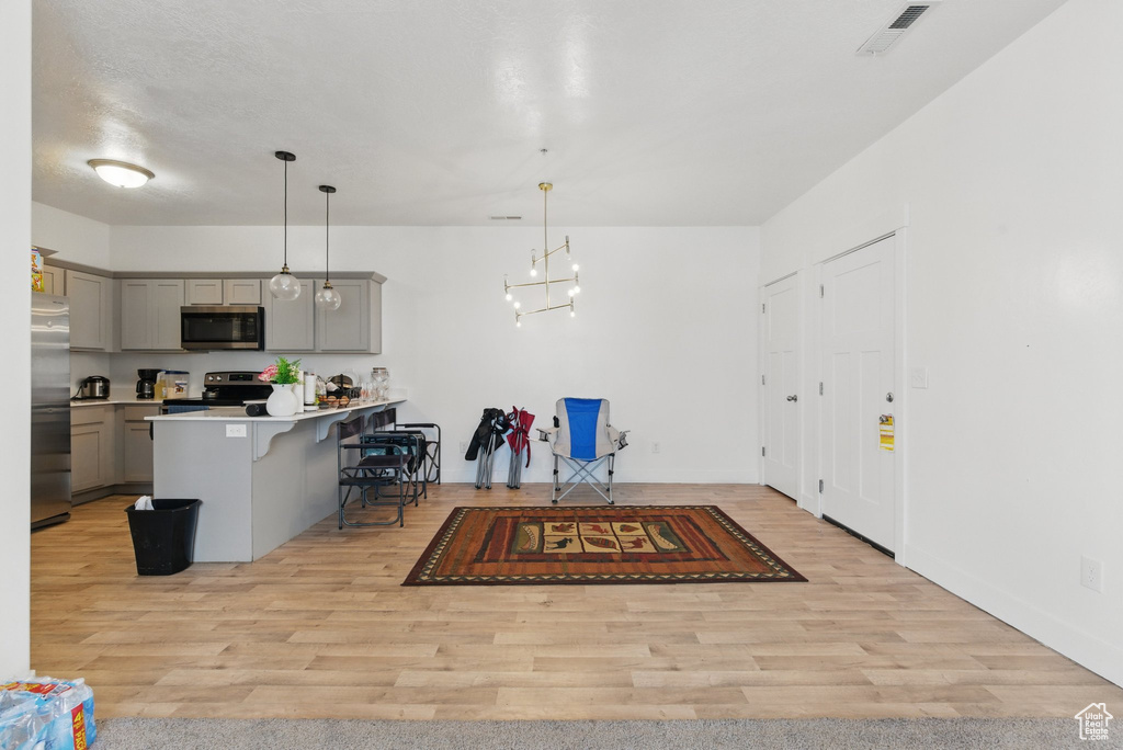 Kitchen featuring gray cabinetry, stainless steel appliances, light wood-style floors, and a kitchen breakfast bar