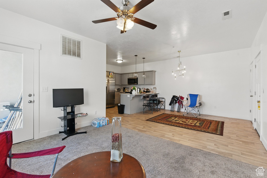Living room with light wood-type flooring, visible vents, ceiling fan with notable chandelier, and baseboards
