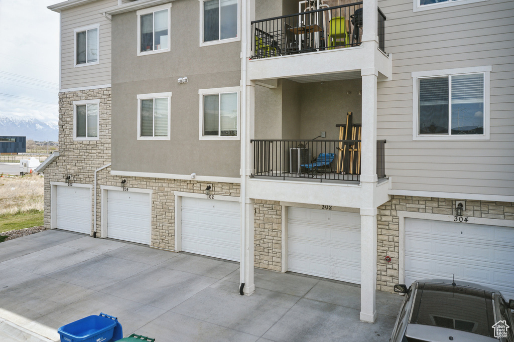 Back of house featuring stucco siding, a garage, driveway, stone siding, and central AC