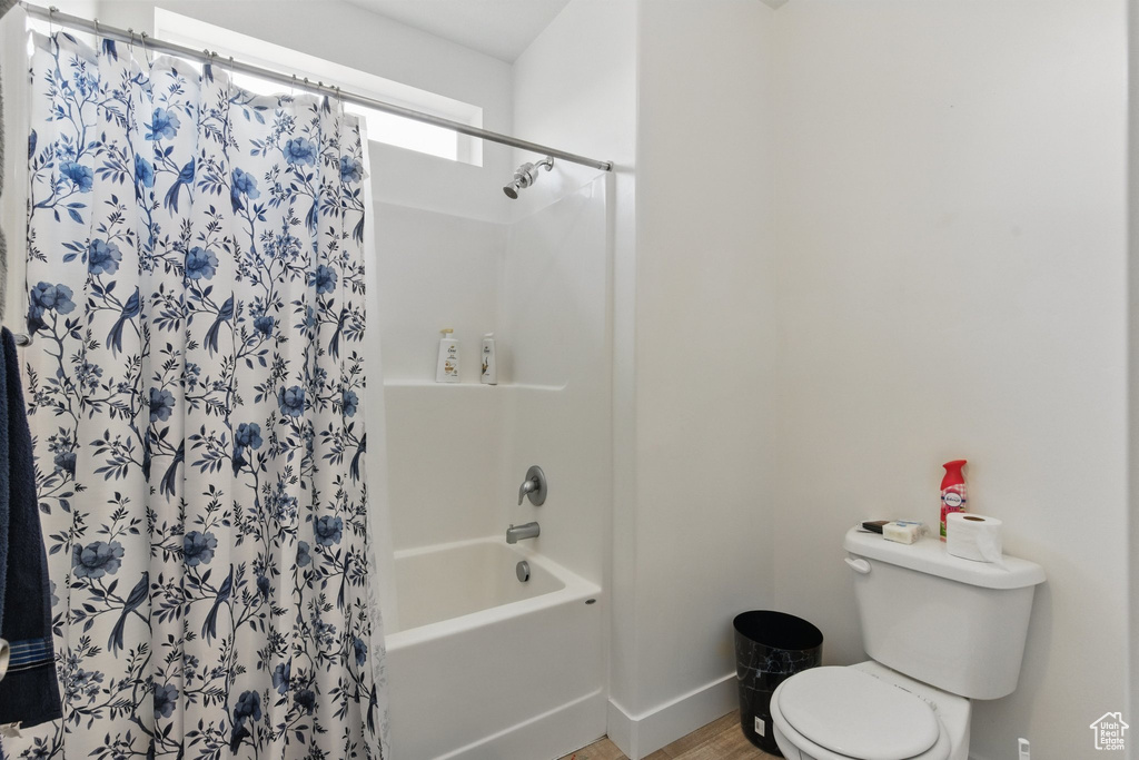 Full bathroom with toilet, shower / bathtub combination with curtain, wood finished floors, and baseboards