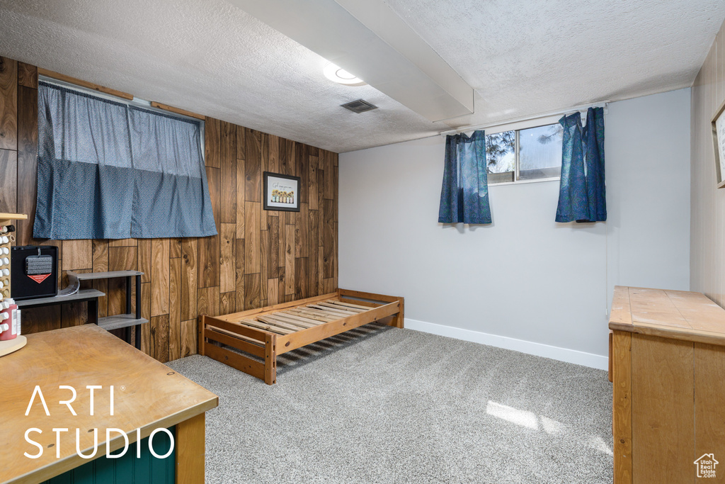 Bedroom with carpet floors, a textured ceiling, wood walls, and visible vents