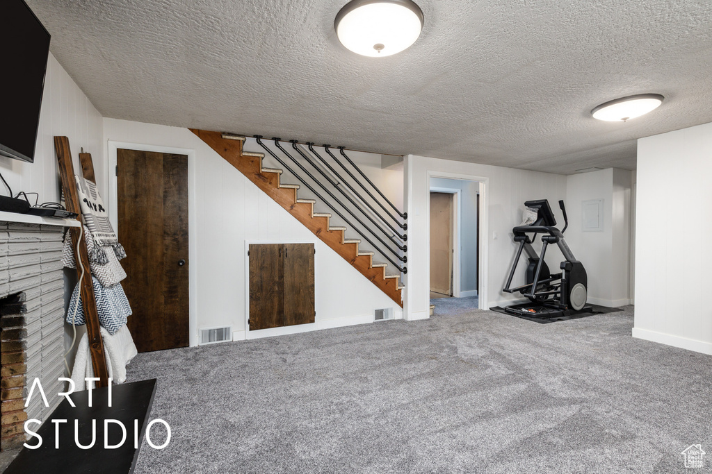 Finished below grade area with a textured ceiling, visible vents, a brick fireplace, stairway, and carpet