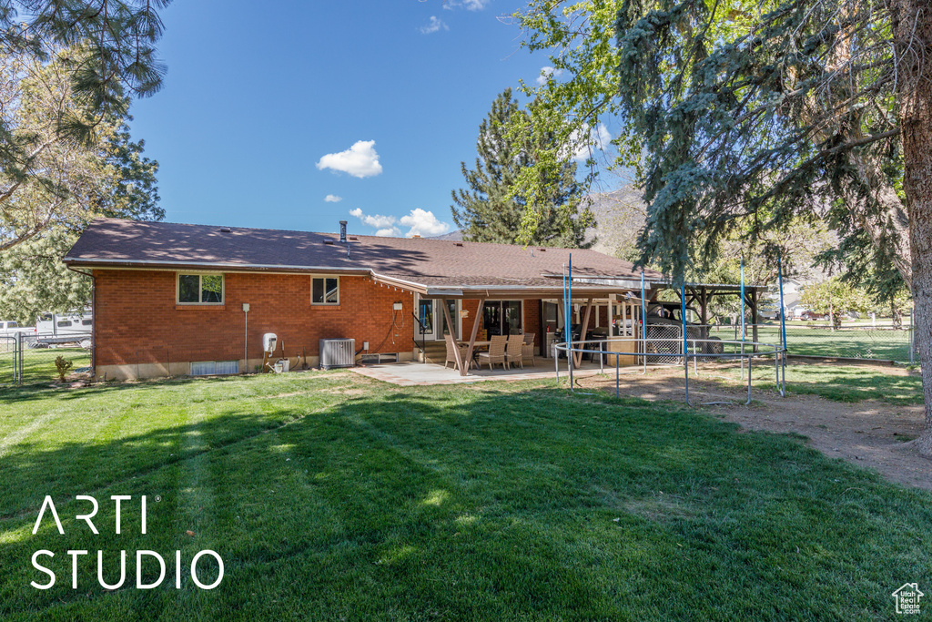 Rear view of house featuring fence, a shingled roof, brick siding, a lawn, and a patio