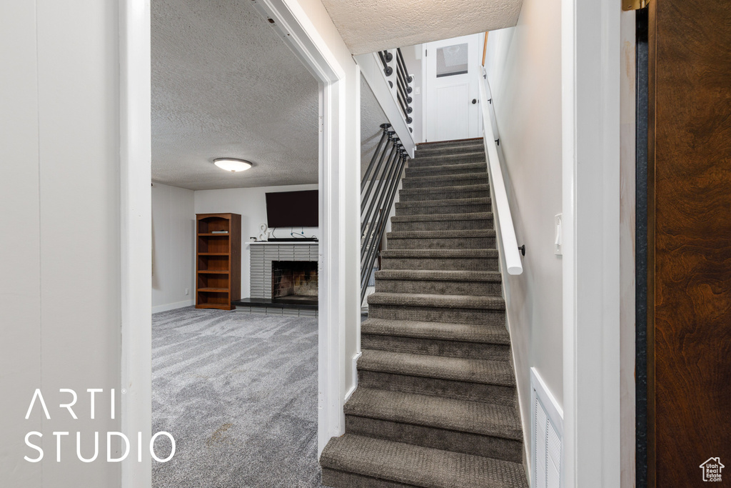 Stairs with carpet floors, visible vents, baseboards, a fireplace with raised hearth, and a textured ceiling