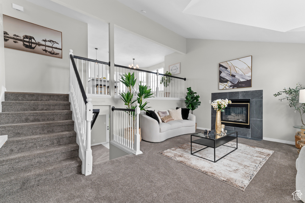 Carpeted living area featuring an inviting chandelier, baseboards, vaulted ceiling with beams, a tile fireplace, and stairway