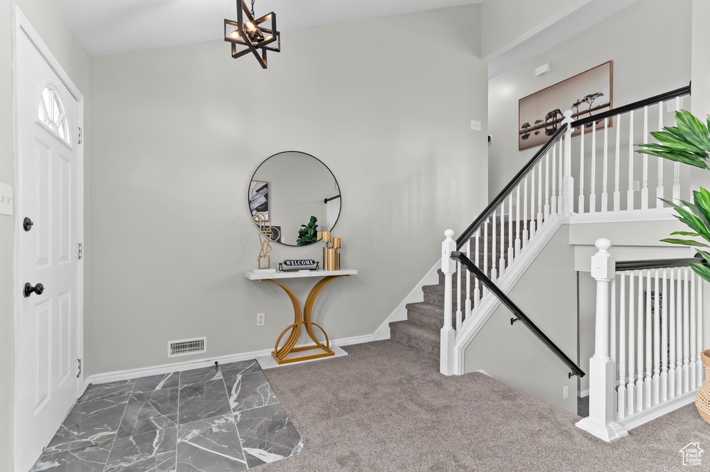 Carpeted entrance foyer with visible vents, baseboards, a chandelier, and stairway