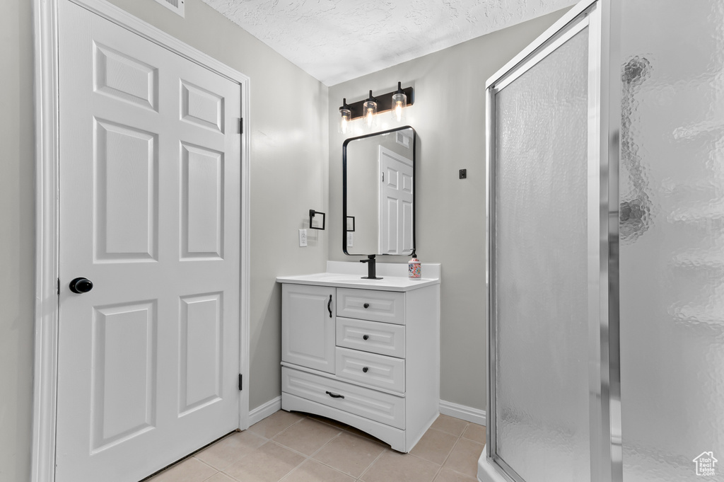Full bathroom with vanity, a textured ceiling, tile patterned floors, baseboards, and a stall shower
