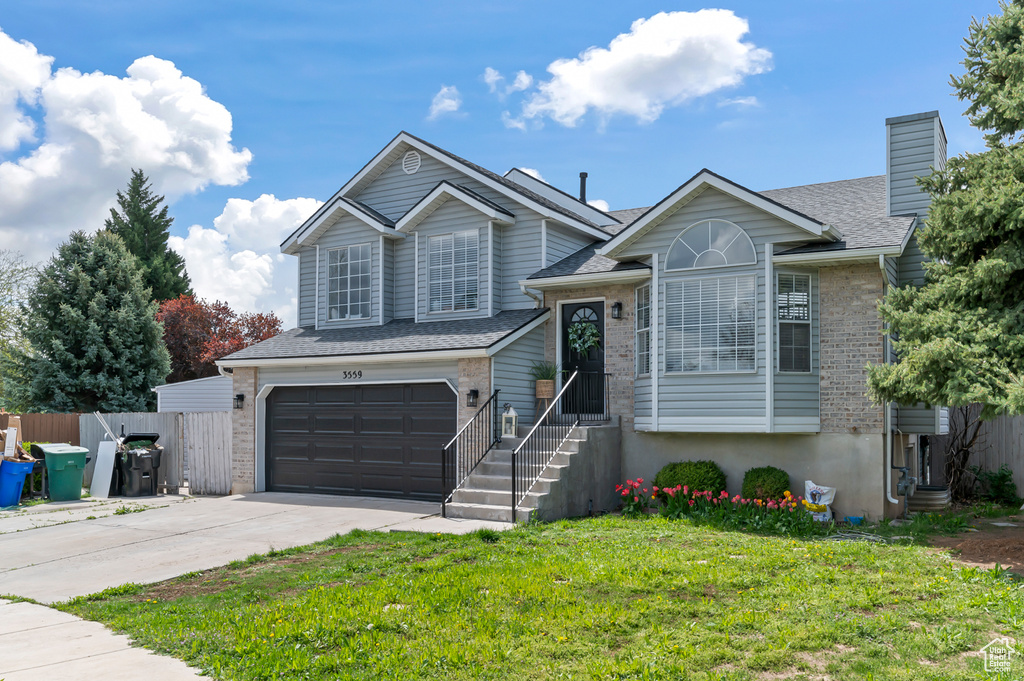Split level home featuring a garage, fence, a front yard, brick siding, and driveway