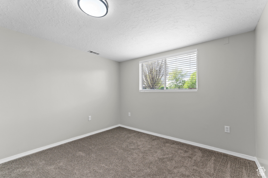 Carpeted spare room with visible vents, a textured ceiling, and baseboards
