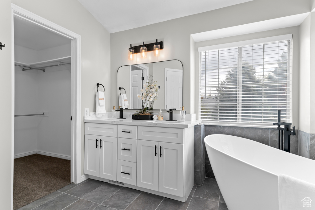 Full bathroom with double vanity, a freestanding bath, a sink, tile patterned floors, and a spacious closet
