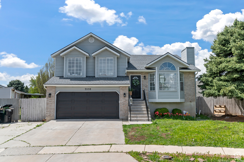 Tri-level home with a garage, fence, a chimney, brick siding, and concrete driveway