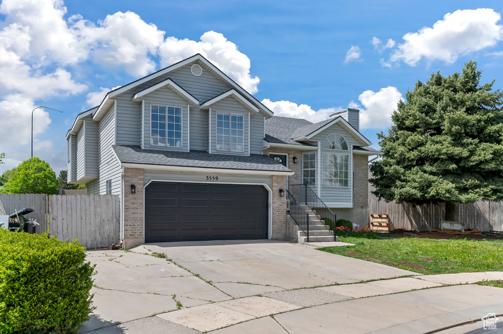 Split level home with brick siding, a garage, fence, and driveway