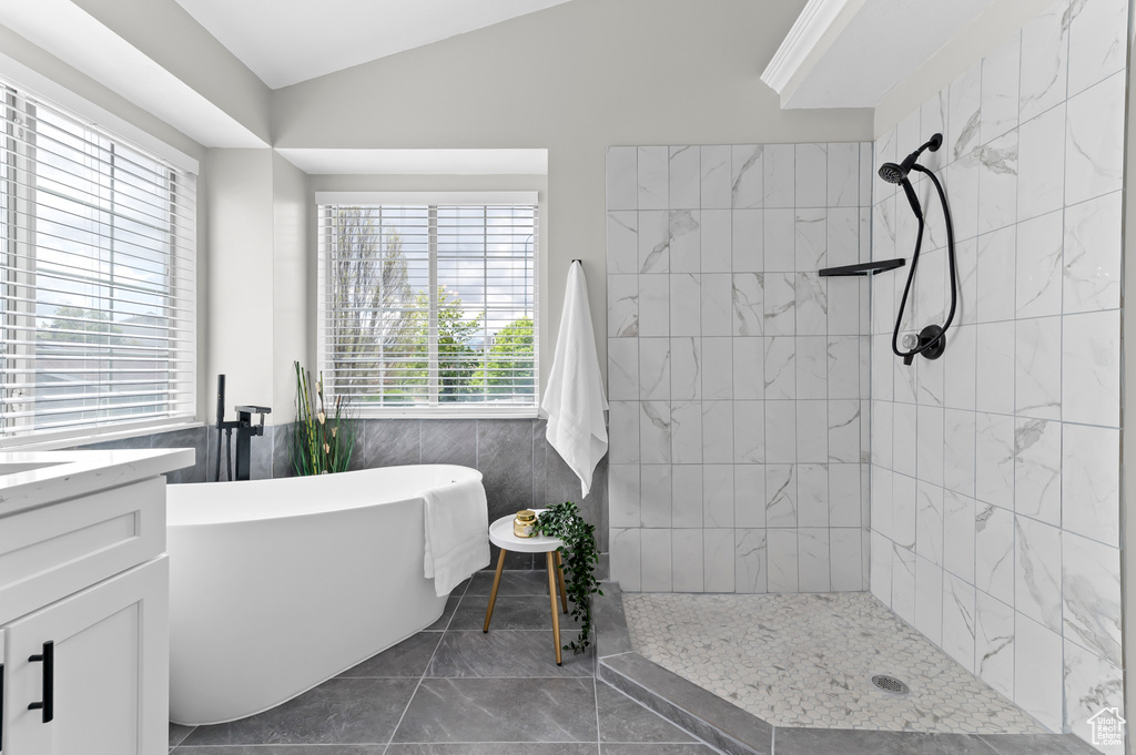 Bathroom featuring a freestanding tub, tile walls, a tile shower, vaulted ceiling, and vanity