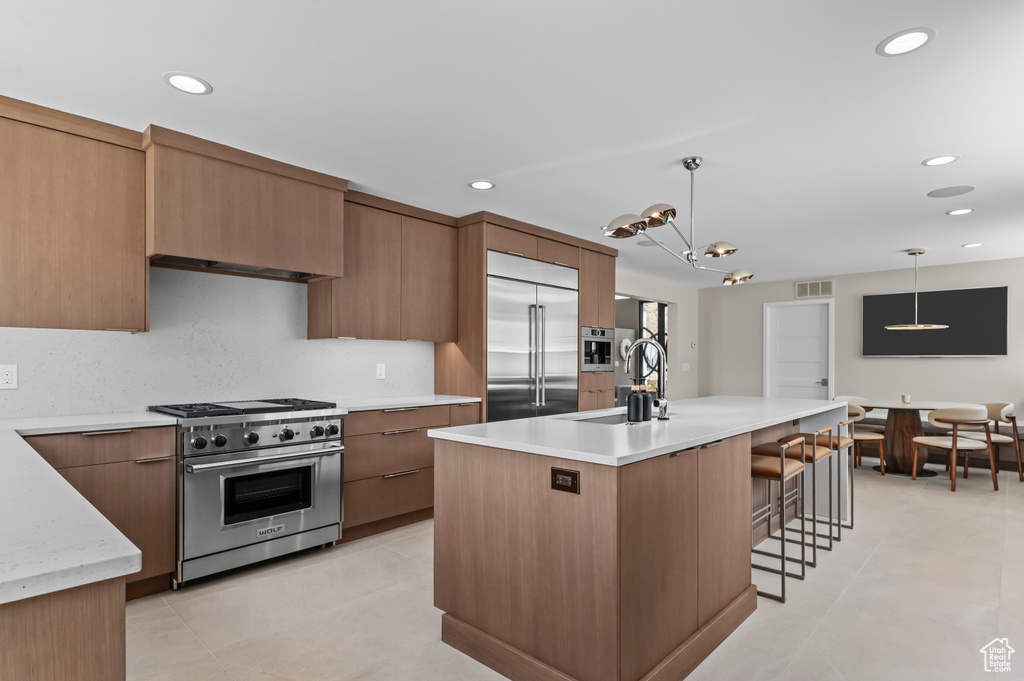 Kitchen featuring high quality appliances, hanging light fixtures, a sink, light countertops, and modern cabinets