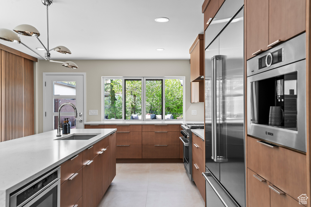 Kitchen featuring brown cabinets, a sink, built in appliances, light tile patterned floors, and modern cabinets
