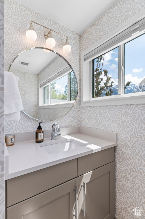 Bathroom with wallpapered walls, visible vents, and vanity