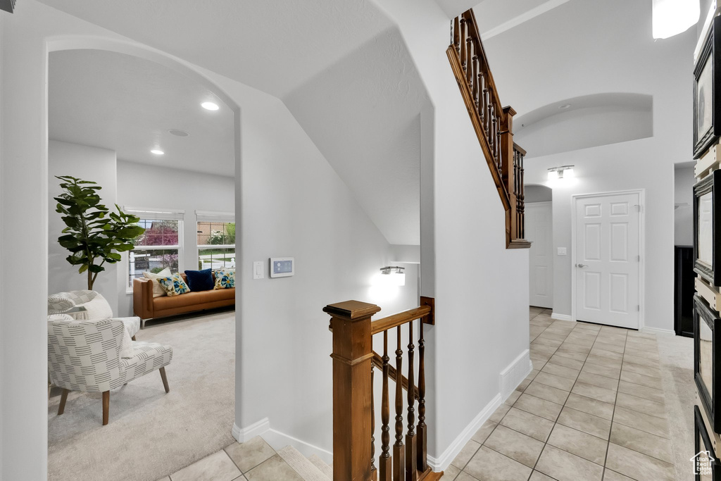 Hallway with arched walkways, vaulted ceiling, light tile patterned floors, light carpet, and recessed lighting