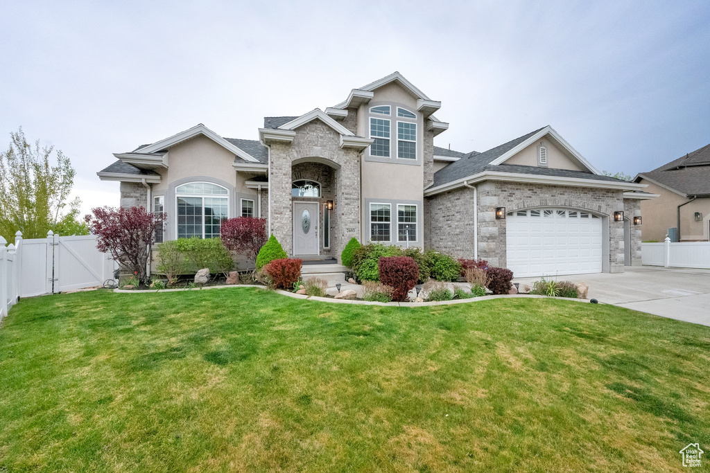 View of front facade featuring fence, stucco siding, driveway, and a front yard