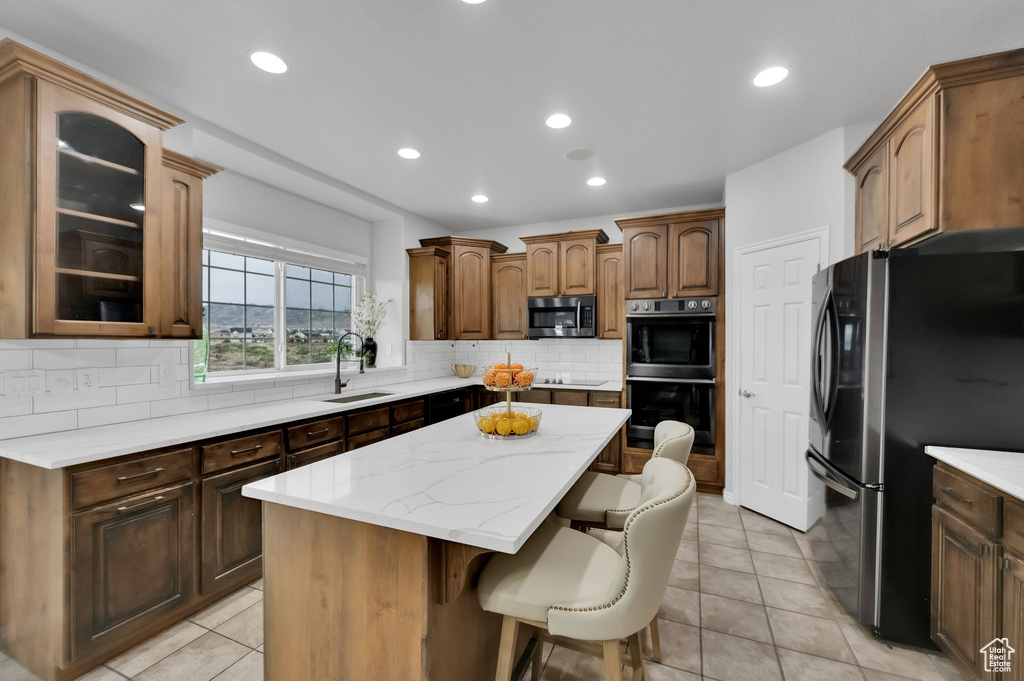 Kitchen featuring freestanding refrigerator, multiple ovens, a center island, stainless steel microwave, and a sink