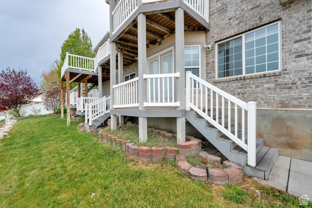 View of side of home with a yard, brick siding, a wooden deck, and stairs