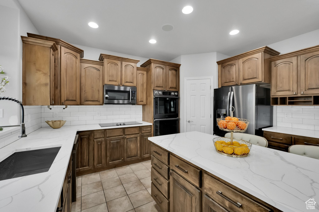 Kitchen featuring a sink, decorative backsplash, light stone countertops, and black appliances