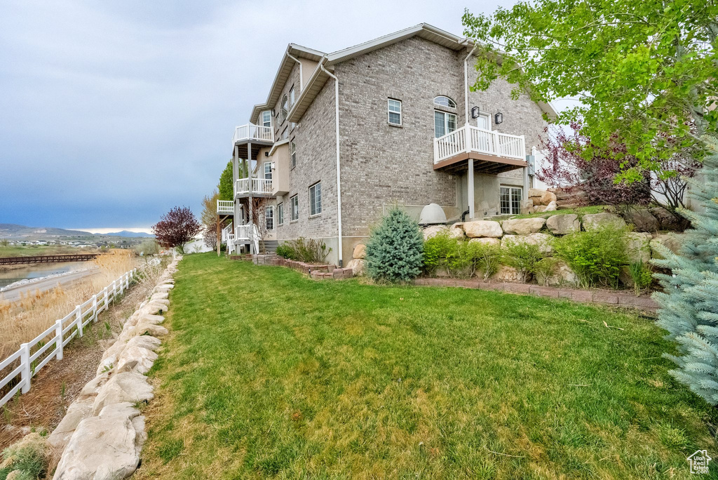 View of property exterior featuring brick siding, a lawn, fence, and a balcony