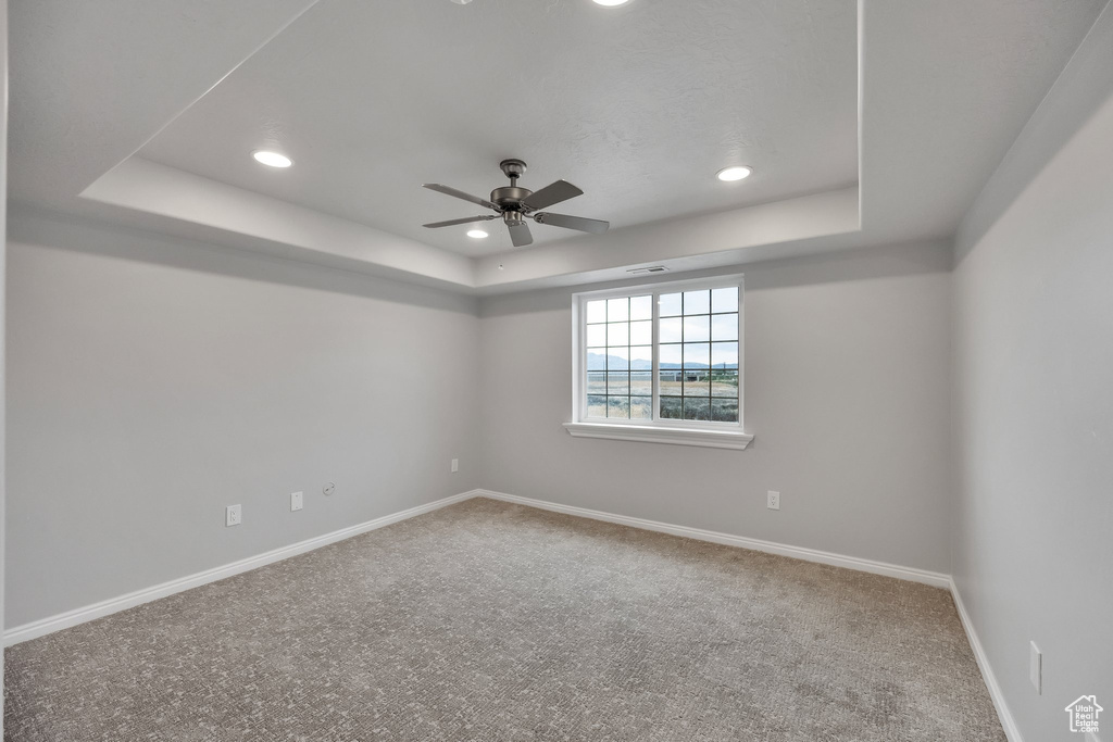 Unfurnished room with carpet floors, ceiling fan, baseboards, and a tray ceiling