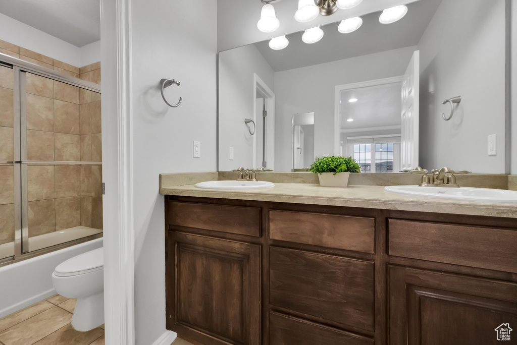 Full bath with double vanity, a sink, combined bath / shower with glass door, and tile patterned floors