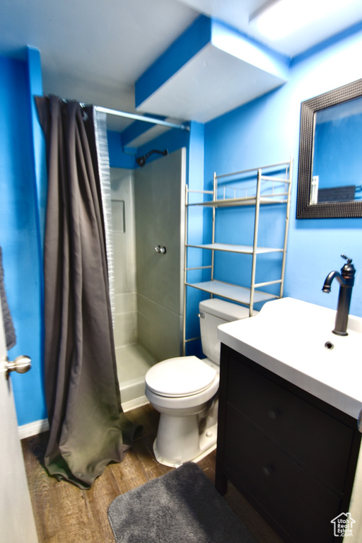 Full bath with toilet, a stall shower, wood finished floors, and vanity