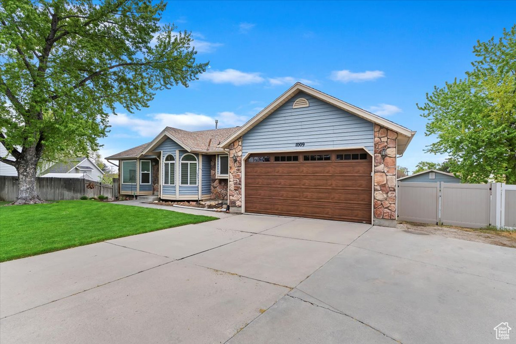 Single story home with driveway, a front yard, fence, an attached garage, and stone siding