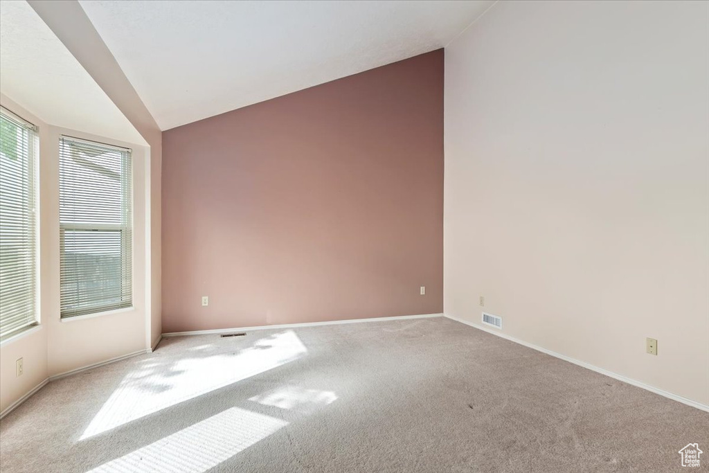 Carpeted spare room featuring baseboards, visible vents, and lofted ceiling