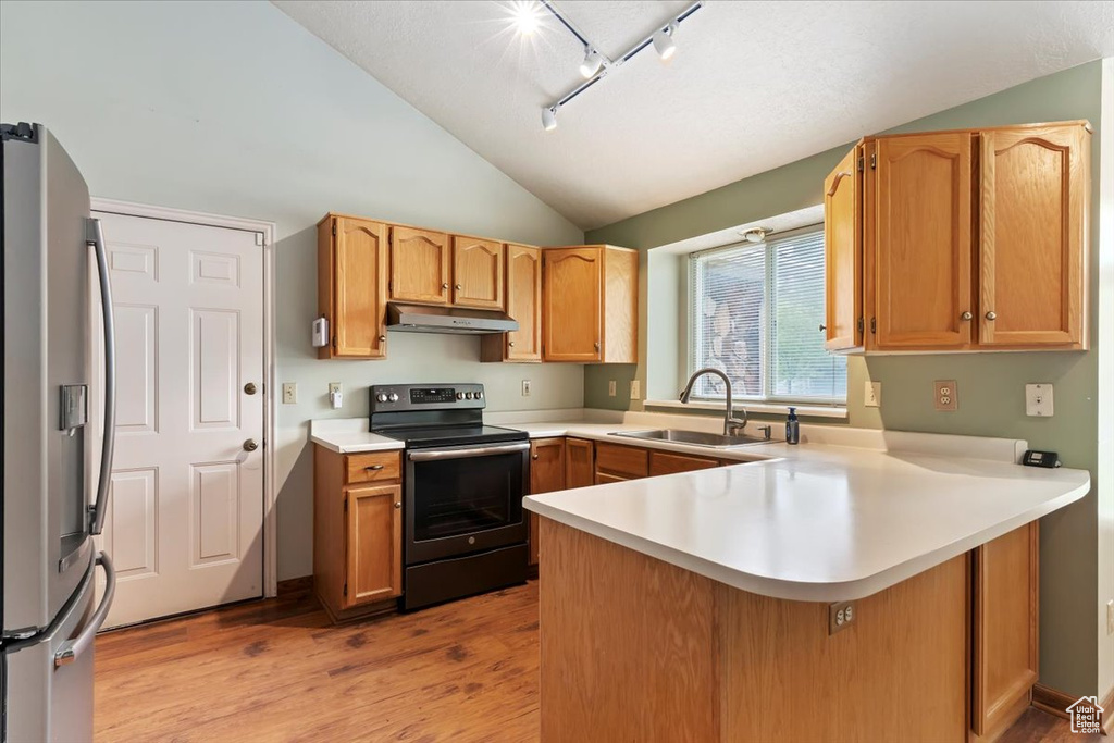 Kitchen featuring electric range, a peninsula, stainless steel refrigerator with ice dispenser, under cabinet range hood, and a sink