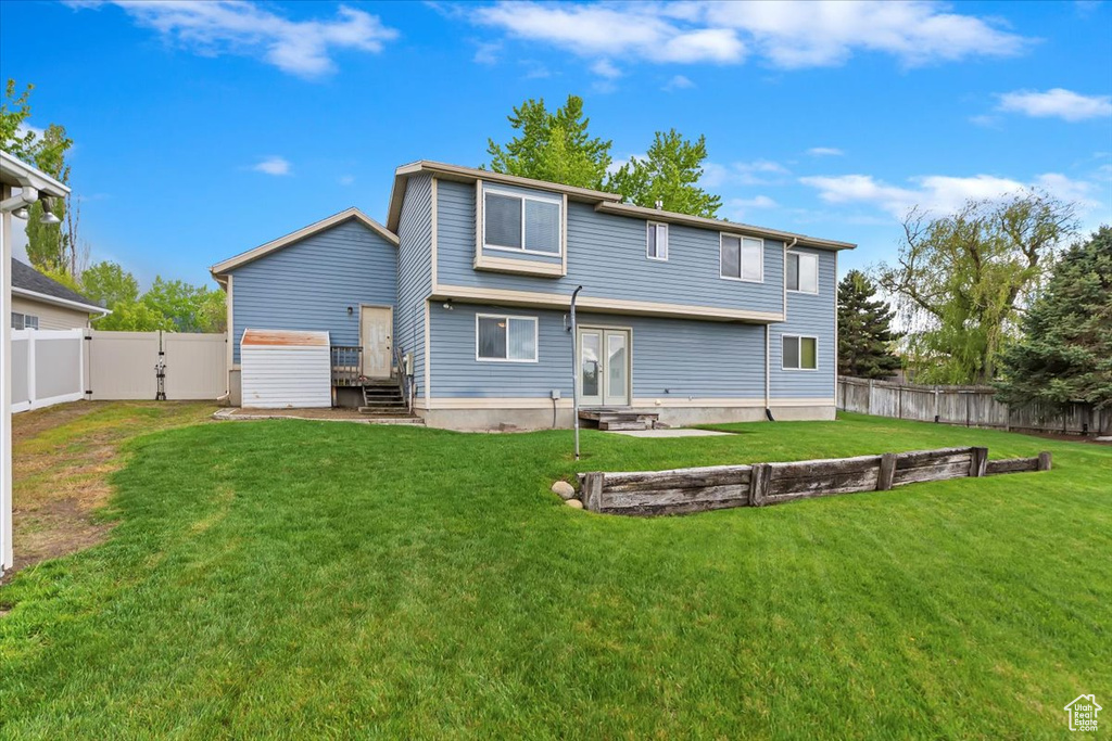 Back of house with a fenced backyard, a gate, and a lawn