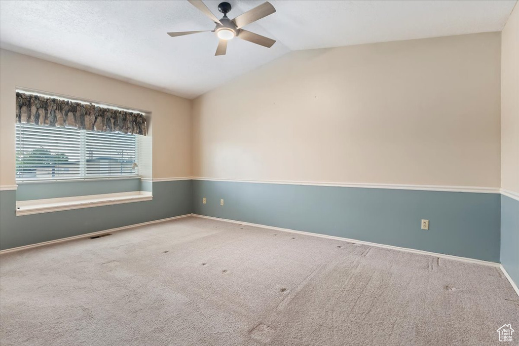 Carpeted spare room featuring baseboards, ceiling fan, visible vents, and lofted ceiling
