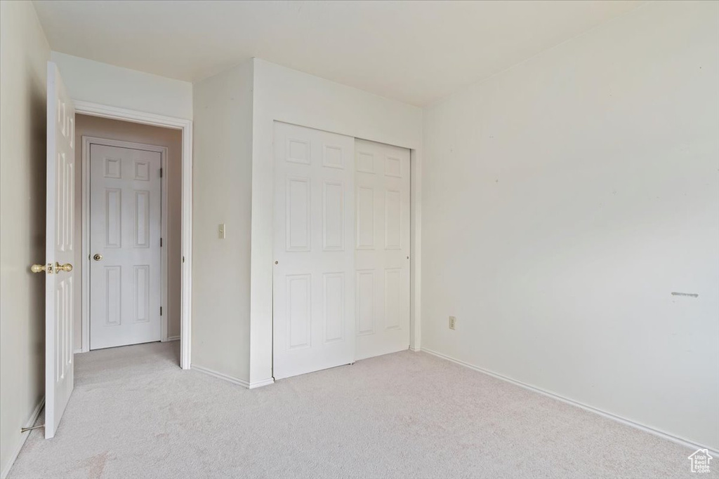 Unfurnished bedroom with baseboards, a closet, and light colored carpet