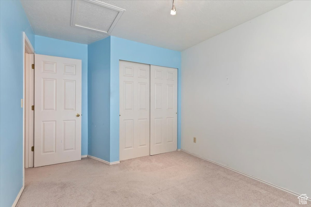 Unfurnished bedroom with baseboards, light carpet, a closet, and attic access