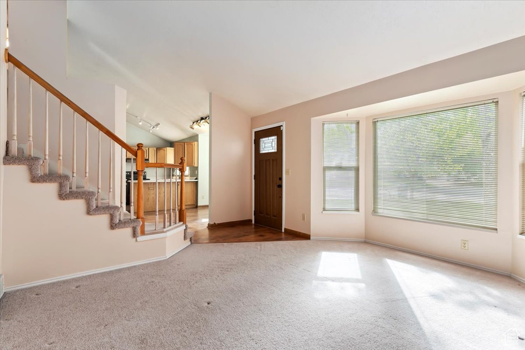 Carpeted entrance foyer with stairs, baseboards, track lighting, and lofted ceiling