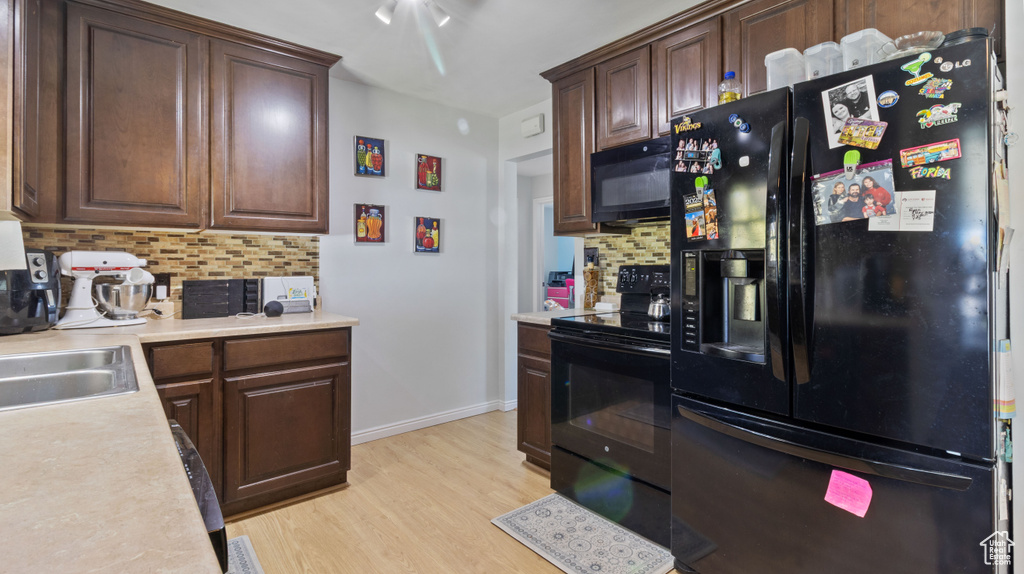 Kitchen with light countertops, light wood-style flooring, backsplash, and black appliances