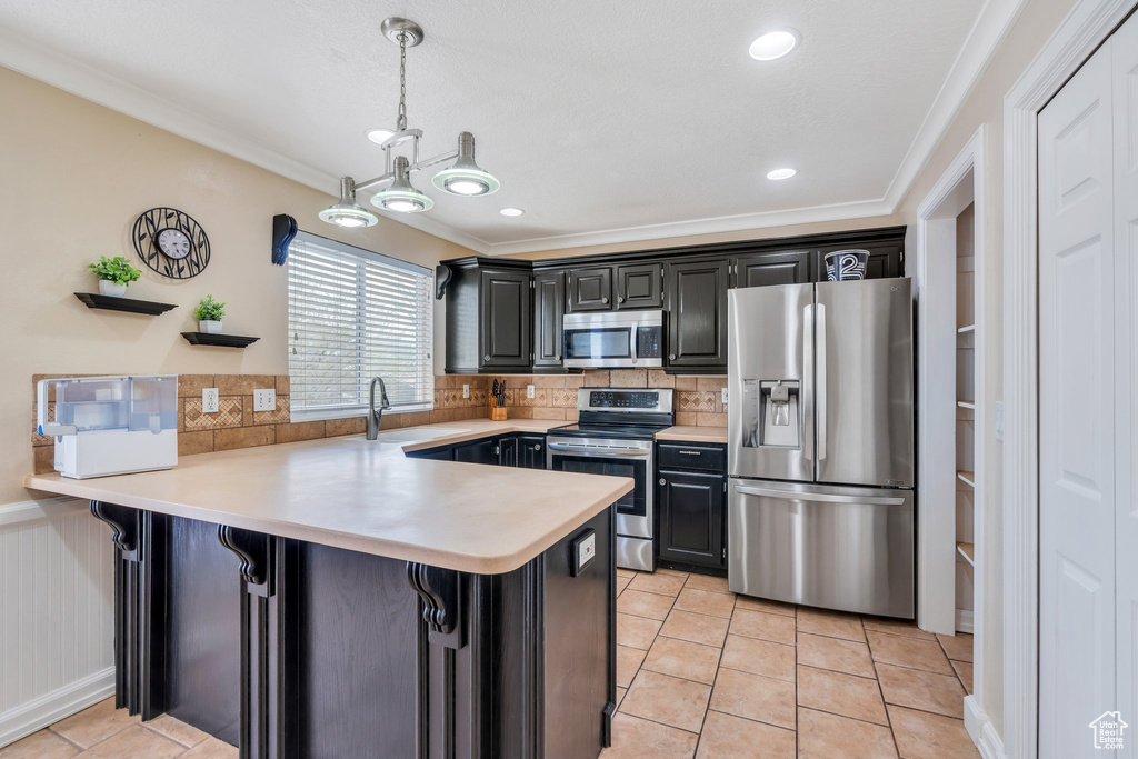 Kitchen featuring ornamental molding, a peninsula, light countertops, a sink, and stainless steel appliances