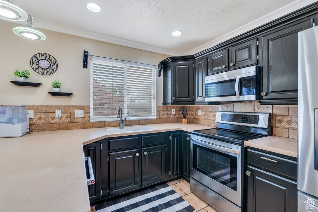 Kitchen with decorative backsplash, a sink, light countertops, dark cabinetry, and stainless steel appliances