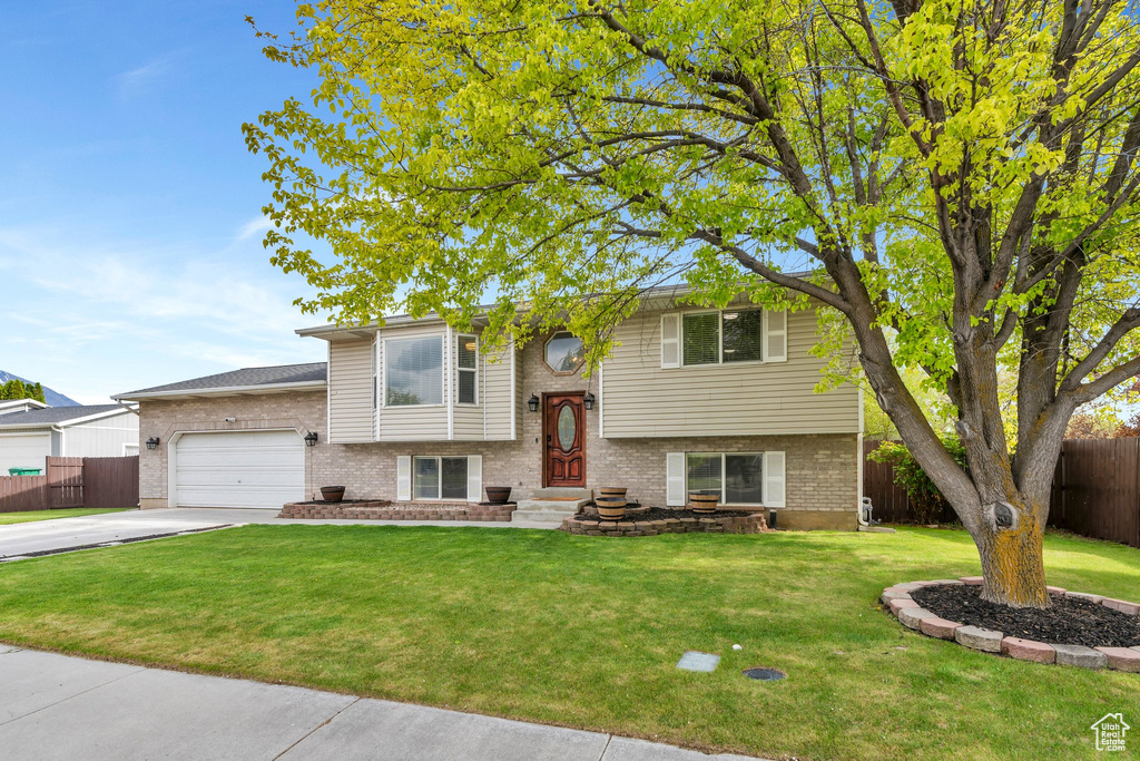 Split foyer home with brick siding, an attached garage, fence, and a front yard