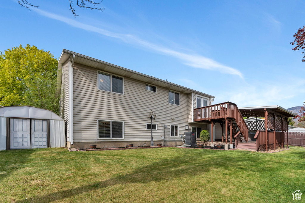 Back of property with a wooden deck, a shed, stairway, an outbuilding, and a lawn